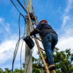 A telecoms worker is shown working from a utility pole ladder